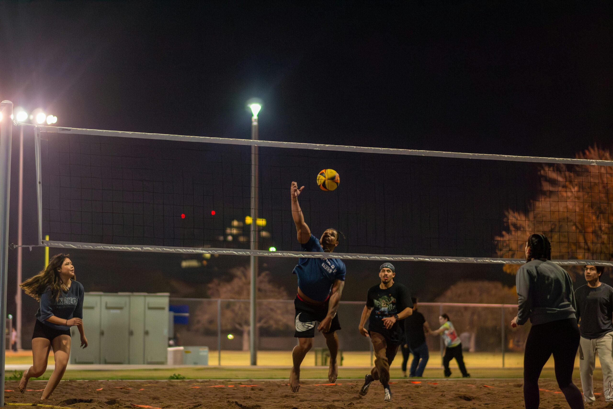 Amateur volleyball players enjoy a dynamic game under the lights in an Arizona park.